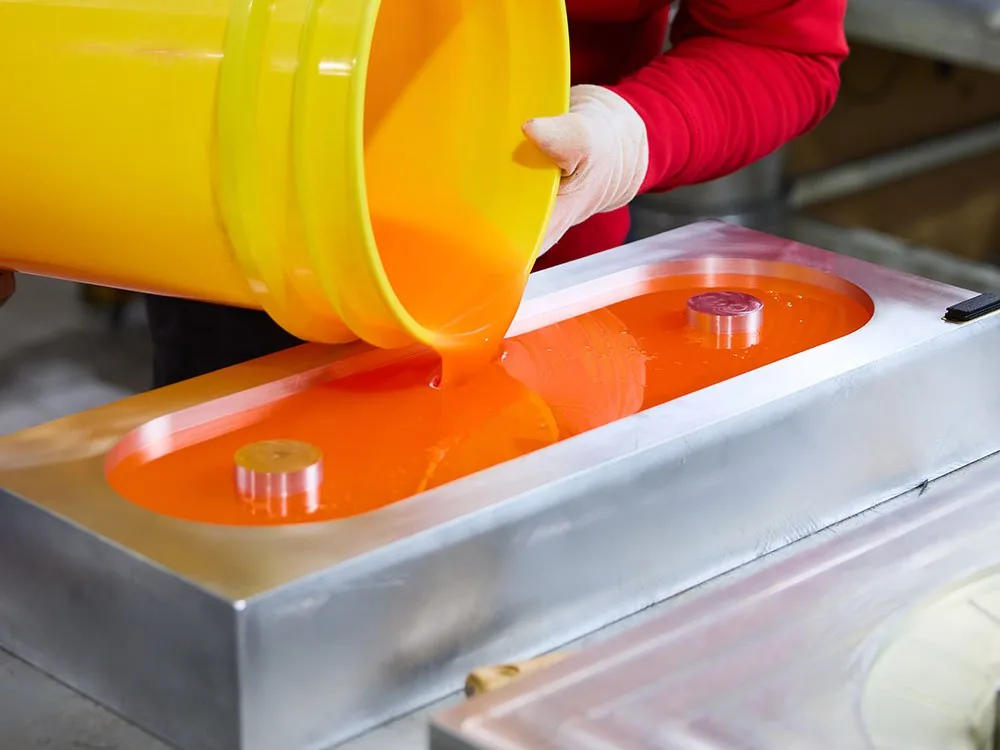 Oranges Polyurethan wird aus einem Eimer in eine Stahlform gegossen